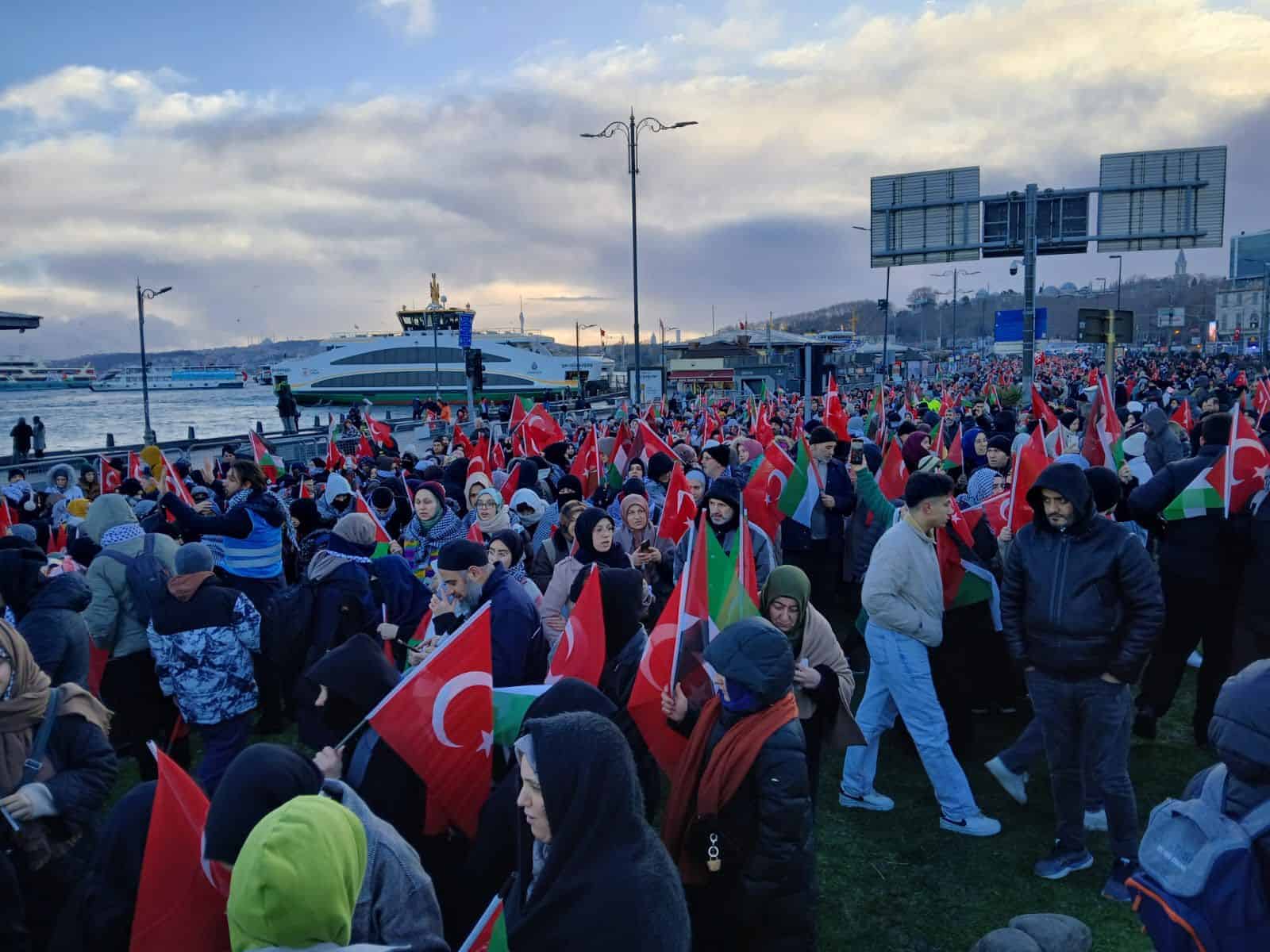 Güzel bir deniz kenarı ortamında, kalabalık vatandaşlar ve bayraklarla dolu sahne.